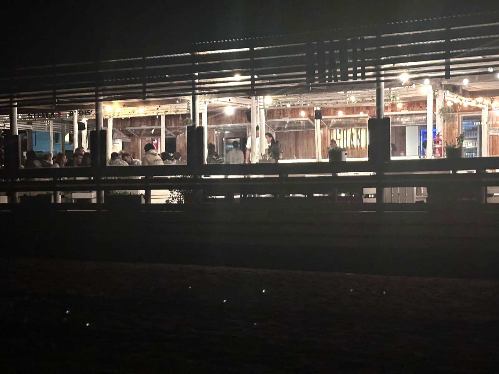 SHANTI de noche: la estructura del deck iluminada, con mesas y luces cálidas en el interior.
